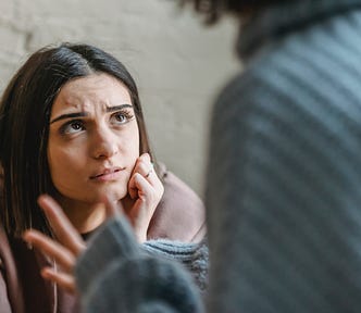 Photo of a woman looking upset and looking up at another woman who is speaking