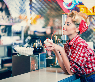 Woman wearning old fashion clothes standing in an old diner drinking strawberry shake.
