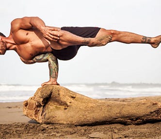 Picture of a man performing a yoga one hand stand on a log at the beach
