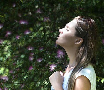 Woman Closing Her Eyes Against Sun Light Standing Near Purple Petaled Flower Plant