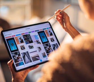 A woman holding a tablet and looking at an array of images on it. She’s holding a tablet pen and about to click on one of them.