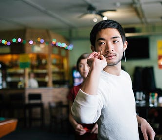 A man prepares to throw a dart with a focused expression.