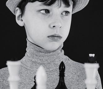 Black and white portrait of a sad young boy at a chess board