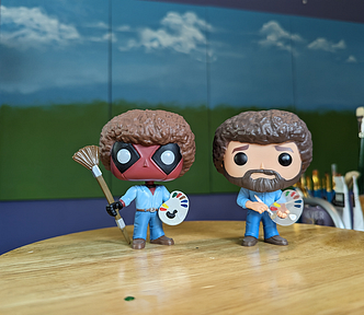 Funko Pop Bob Ross and Deadpool Bob Ross figurines placed in an art studio in front of a large 4 panel painting as inspiration for the artist herself. Which is me. Kathy LaFollett. Kathy LaFollett Murals and Canvas