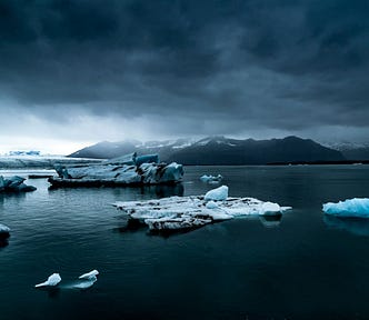 Small icebergs floating in the ocean under dark, cloudy skies.