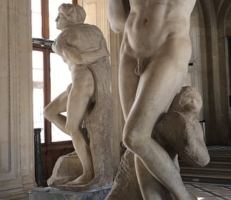 2 male marble figures emerging from their blocks. Bands around their chests. Facial expression is peaceful resignation.