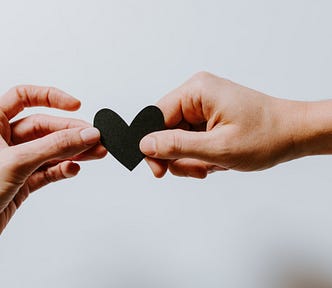 Two hands holding a blue heart shaped piece of card