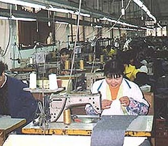 Two rows of industrial sewing machines extending backwards in a factory in China. The first two machines are being operated by a man and a woman who are smiling as they work.