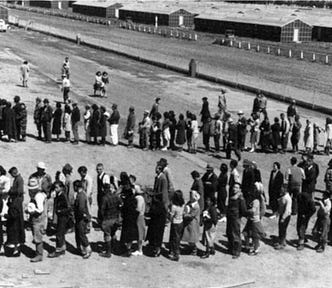 A black-and-white photograph of two lines of Japanese Americans waiting to be processed at an internment center