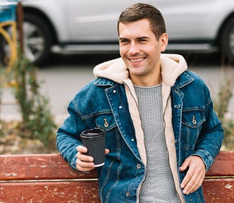 A smiling man sits on a bench with a coffee cup in his hand.