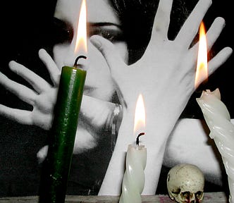 witchy-looking woman with her hands splayed in front of her face and candles in the foreground (once and future witches)