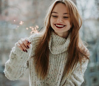 Woman in white long sleeved sweater holding a sparkle