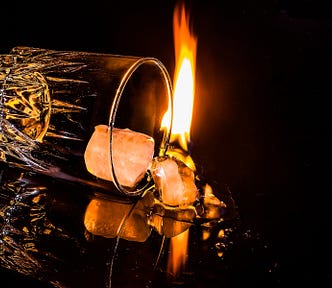 black background aglow with flames, spilled over hi-ball glass with ice falling out
