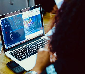 Html 5 codes are displayed on a MacBook screen. Next to the MacBook are two mobile devices sitting on a table.