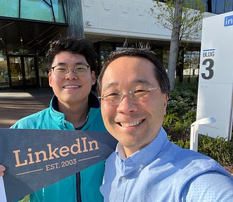 Two men in front of LinkedIn office building holding a sign that says “LinkedIn est. 2023"