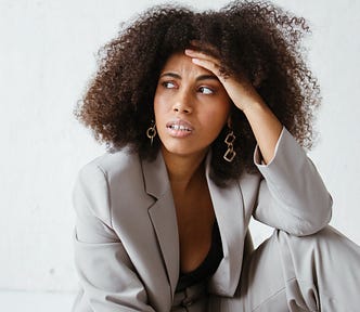 A woman with an afro wearing a pantsuit looks away from the camera, frustrated AF