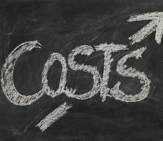 IMAGE: The word “Costs” written with chalk on a blackboard, with a diagonal arrow pointing upwards