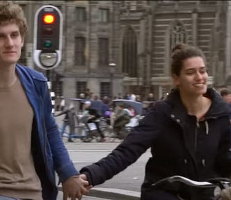 Two bike riders with out helmets holding hands, with bikes in the background.