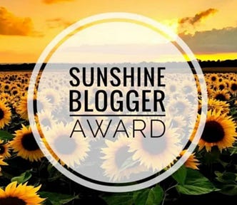 Golden sunflower field under a sunset sky with a circular ‘Sunshine Blogger Award’ logo in the center.