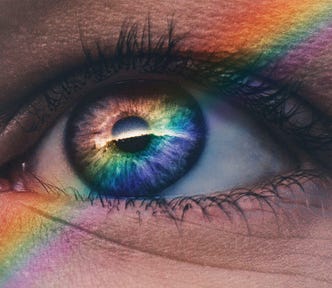A close-up of an eye with a rainbow stripe of light overlapping it.