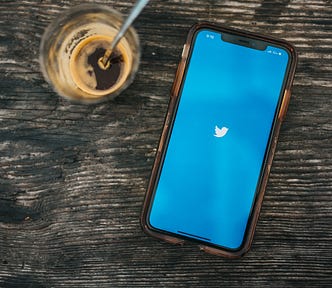 Photo by Nathan Dumlao on Unsplash. A mobile phone with a Twitter logo on its screen laying flat on a desk next to an espresso