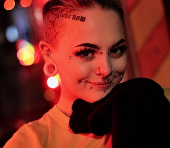 Woman with multiple facial piercings smiles at camera.