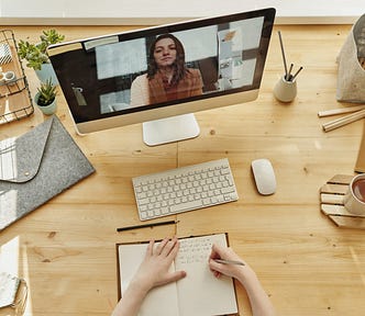 A student sitting at a minimal natural wooden desk watching an online course while taking notes.