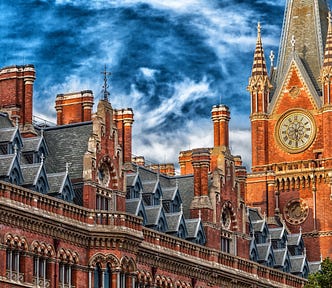 Sunlit clocktower made of russet brick against a blue sky with swirling white clouds in the United Kingdom.