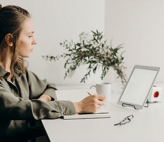 woman in gray short using iPad and writing in notebook