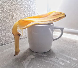A coffee cup with a banana peel on top, sits on a concrete surface with a backlight.