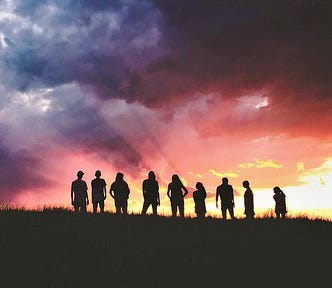 silhouette of group of people standing on hillside with colorful sunset sky behind them