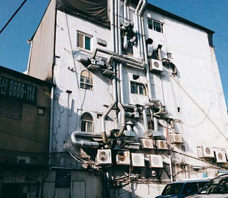 A building with a complicated mess of air ducts and air conditioners bolted to the outside.