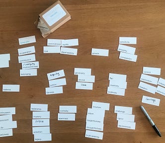 About 50 small white cards with typed and handwritten words on them, on a table, with a Sharpie pen