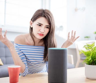 A woman sitting in a living room looks at her smart speaker with disdain and raises her hands in frustration.
