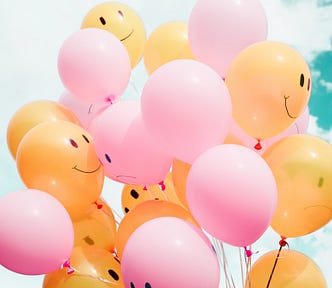 Pink and orange balloons, some with happy faces, some with sad faces drawn on them
