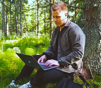 A man sitting on the ground uses his laptop in the woods