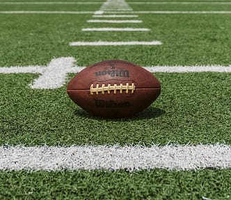 A football sites on a football field, green grass and white lines are under the football.