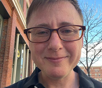 The author is smiling into the camera. He is white and trans. He looks a little tired, but otherwise relaxed. He’s wearing glasses.