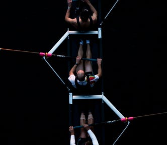Overhead view of four rowers in a racing shell on dark water, each holding oars with pink handles, captured in strong contrast with the black background.