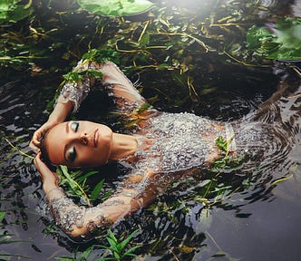 Beautiful woman is immersed in water on her back in seaweed. She is face up, eyes closed. Beautiful makeup, elbows bent, hands resting on the top of her head. Magic, beauty, fantasy aesthetic. Captivating.