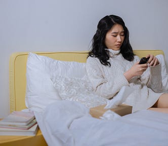 Woman in white sweatshirt sitting on bed.