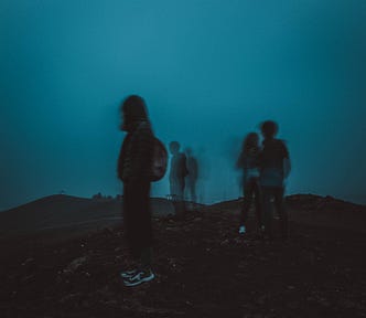 Five blurry silhouettes standing on a hill in front of a dark teal sky