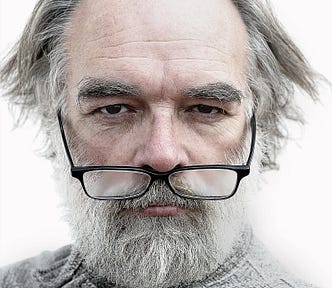 Picture of a grumpy looking old man with an almost bald head and his glasses hanging beneath his nose.