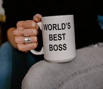 Hand of a woman in black holding white ceramic mug with the text “World’s Best Boss”.