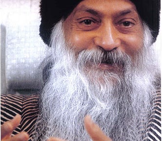 This is photo of a man in long white beard and moustache. His eyes sparkle and he’s smiling. His hands convey this expression of something meaningful that he is sharing with his audience. He’s dressed in a black hat and at tweed jacket.