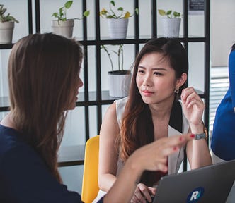 Two women having a conversation sitting infront of a laptop
