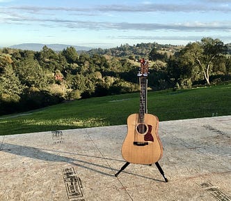 acoustic guitar sitting on the subfloor of a house about to be built, with expansive view of mountains in background