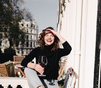 Happy smiling woman with red wine on balcony fence