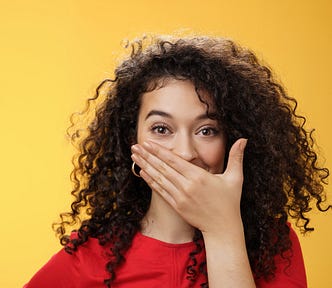 Closeup shot of excited and happy attractive female with curly hair giggling chuckling and covering her mouth