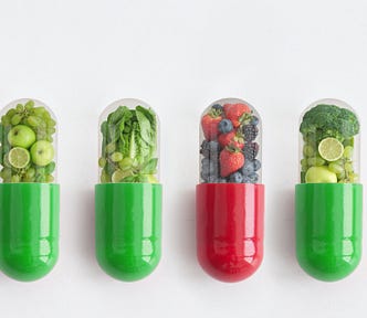 Four vitamins, with the upper half of each clear and filled with either tiny fruits or vegetables.